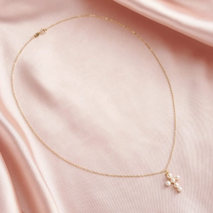 Detail of cross pearl pendant necklace with gold chain on pink satin fabric background