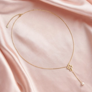 Détail du pendentif croix dorée avec perle blanche sur fond de soie rose luxueuse