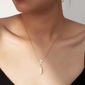 Elegant gold cross necklace with a white baroque pearl pendant shown on a model
