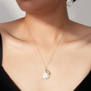 Collier en perles baroques avec pendentif croix évidée doré porté par un modèle