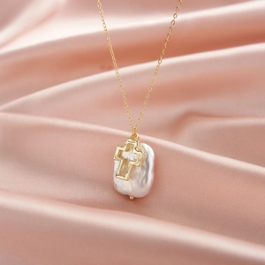 Collier perle baroque avec pendentif croix dorée ajourée sur élégant tissu en soie rose