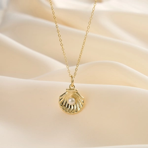 Détail macro du pendentif coquillage doré avec perle sur fond de satin crème luxueux