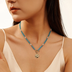 Turquoise beads and pearl necklace with a gold shell pendant on a silk-clad model
