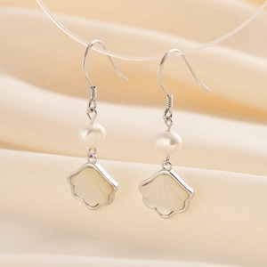 Detail of 14K gold pearl earrings with shell pendants on elegant beige satin backdrop