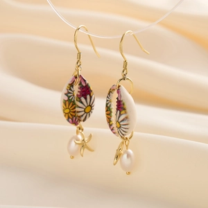 Detailed view of daisy painted shell earrings with starfish charms and white teardrop pearls