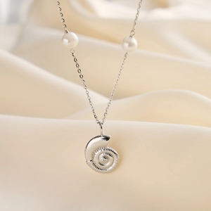 Detail of silver conch pendant necklace with elegant pearls on soft satin background