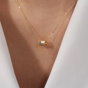 Close-up of golden honeycomb cylinder pendant necklace worn on a female neck
