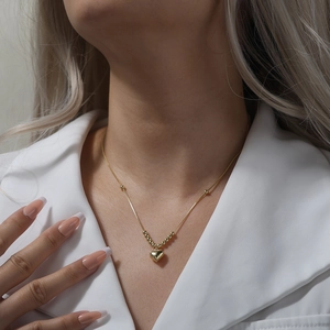 Close-up of a delicate gold heart pendant necklace on a model wearing a white shirt