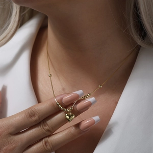 Detailed view of a gold heart pendant necklace with beads on a delicate chain worn by model