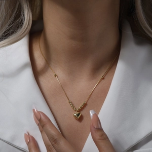 Close-up of a polished gold heart pendant necklace worn on a white suit jacket collar