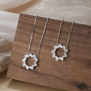 Silver and gold circular necklaces with baguette-cut zircons on walnut display