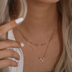 Détail du collier superposé doré avec ailes d'ange et pierre précieuse en goutte