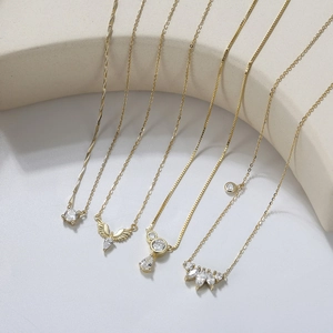 Détail de cinq colliers ailes d'ange plaqués or avec zircons sur un présentoir beige clair