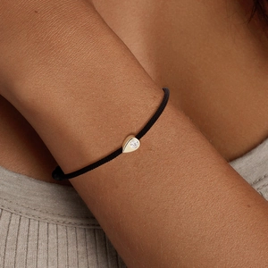 Close-up of a 14K gold teardrop charm with a zircon stone on a black braided bracelet