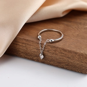 Detail of silver chain ring featuring heart tassel charm on dark wood and silk backdrop