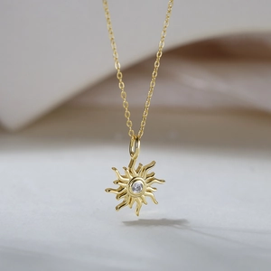 Gros plan du pendentif tournesol doré avec zircon central sur une chaîne délicate