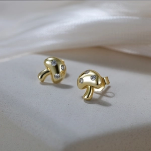 Close-up of gold mushroom studs with zircon inlay on a textured stone surface