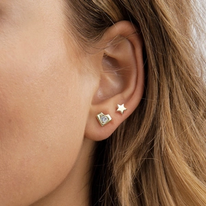 Close-up of gold heart zircon and star stud earrings worn on a model's ear