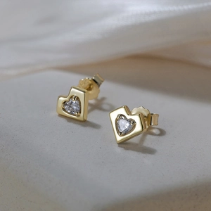 Detail of heart-shaped zircon earrings in gold finish on silk background