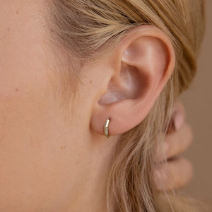 Close-up of mini gold geometric hoop earring with sparkling zircon stones on ear
