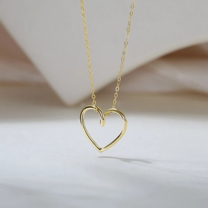 Vue macro d'un pendentif cœur creux en or sur une chaîne délicate avec un fond minimaliste