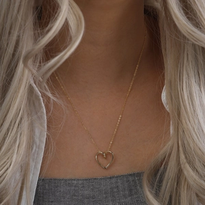 Vue détaillée d'un collier pendentif cœur doré minimaliste porté par un mannequin chic