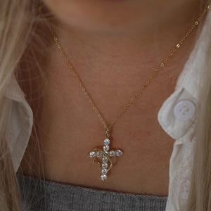 Close-up of gold cross pendant necklace with clear zircons worn by model on white shirt
