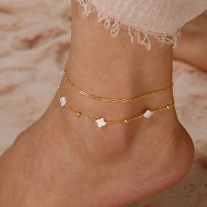 Nahaufnahme eines doppellagigen Gold-Fußkettchens mit Kleeblatt und Strand-Resort-Ästhetik