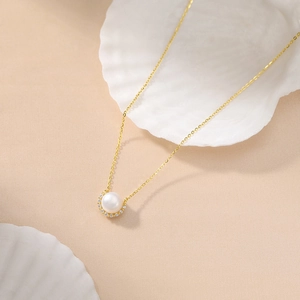 Elegant pearl necklace with gold pave zircon pendant displayed on white sea shells