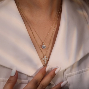Close-up of layered gold necklaces featuring a classic zircon pendant and a cross charm