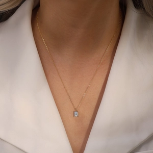 Close-up of emerald cut zircon pendant on a gold chain worn over a white blazer