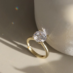 Macro shot of a gold-finish ring with a four-prong set round zircon on a matte background