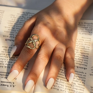 Retro-Ring mit 14k Vergoldung und Kleeblatt-Motiv, getragen über einem Vintage-Buch