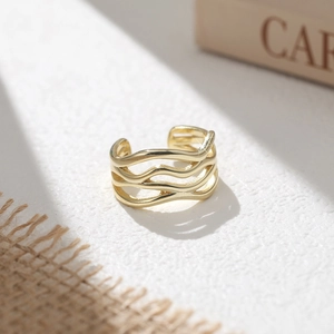 Detailaufnahme eines minimalistischen, goldfarbenen dreilagigen Wellenrings auf Steinplatte