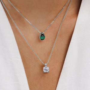 Close-up of layered silver necklaces with pear-shaped green and square clear pendants