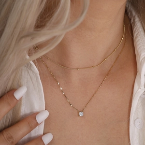 Detail of layered gold beaded and flat twisted chains with a square zircon pendant