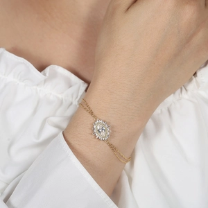 Close-up of a gold double-chain bracelet featuring a marquise-cut crystal and diamond halo