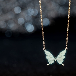 Elegant gold butterfly necklace with luminous blue wings against a dreamy bokeh background