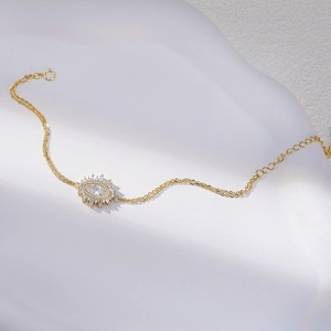 Close-up of golden adjustable evil eye bracelet with marquise-cut crystal on white texture