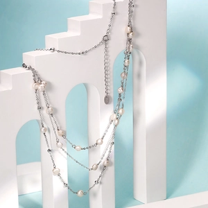 Collier double rang en perles d'eau douce et argent S925 sur un support géométrique blanc