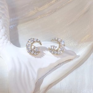 Macro shot of gold crescent moon stud earrings with sparkling pavé crystals on white silk