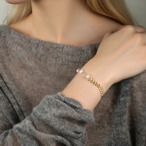 Elegant gold leaf-shaped bracelet with three white pearls worn on a grey knit sweater