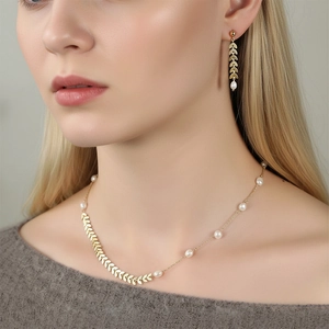 Gold wheat ear necklace and pearl earrings set worn by a model for a chic look