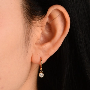 Close-up of gold drop earring with a single round zircon stone worn on an ear