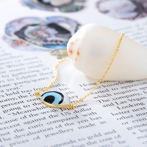Détail du bracelet œil maléfique plaqué or 14K sur coquillage blanc avec breloque émail