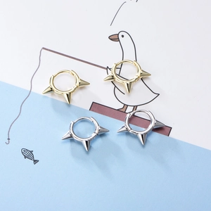 Dettaglio di orecchini a punta oro e argento in stile punk su sfondo minimalista