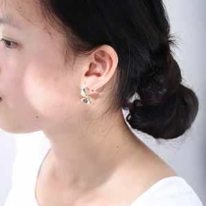 Close-up of a model wearing twisted ribbon gold-plated stud earrings in a glossy finish