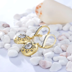 Macro detail of matte 14K gold-plated drop earrings with square zircon on white pebbles