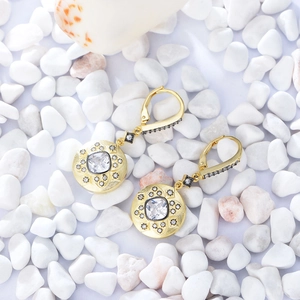 Macro detail of vintage 14K gold-plated drop earrings with square zircon on white pebbles