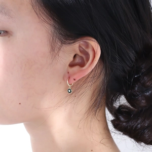 Close-up of a gold C-shape hoop earring with black drip oil finish and center crystal